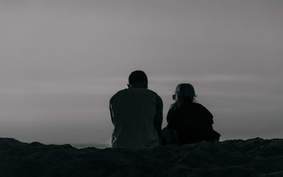 Rear view of couple sitting on railing against sky during sunset