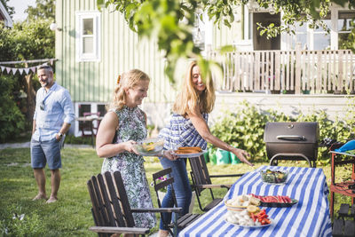 Female friends arranging food on table for social gathering in backyard during summer weekend