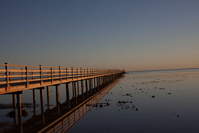 Pier on sea against clear sky during sunset