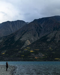 Woman standing at lakeshore against mountains