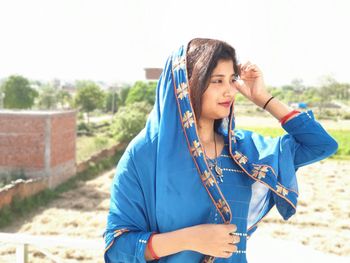 Young woman wearing traditional clothing looking away while standing against sky