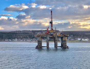 Drilling rig in sea against sky during sunset