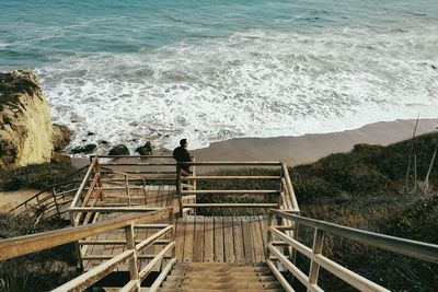 High angle view of man standing on wooden staircase at beach