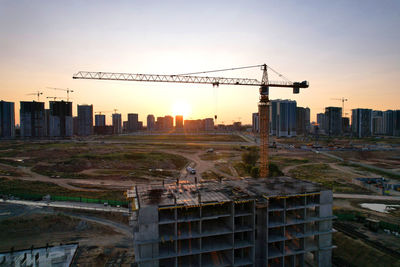 Construction site by buildings against sky during sunset