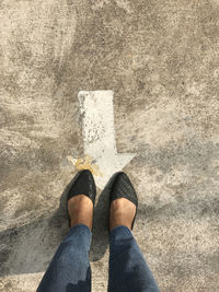 Low section of woman standing by arrow sign on road