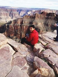 Smiling man using digital tablet while sitting on rocky mountain