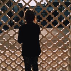 Rear view of young woman standing by patterned window