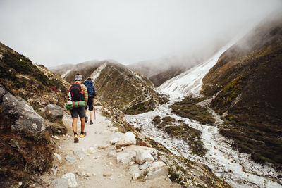 Rear view of friends with backpacks hiking at sagarmatha national park during foggy weather