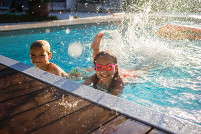 Kids in laugh play in swimming pool at sunny day, refresh at heat weather, active summer vacation