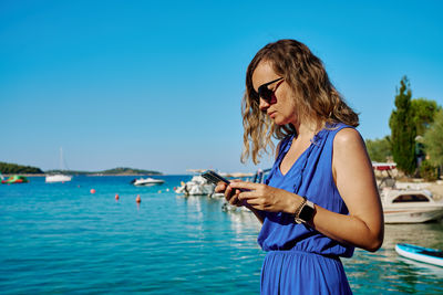 Side view of young woman using mobile phone against sky