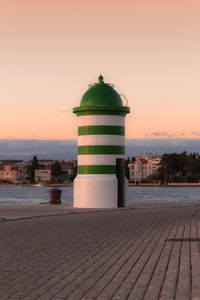 Lighthouse by sea against sky during sunset