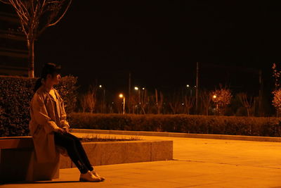 Woman sitting at illuminated city against sky at night