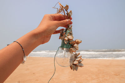 Person holding garbage on beach against sky