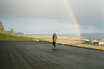 Rear view of man standing on road against rainbow in sky