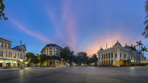 Street by buildings against sky at sunset