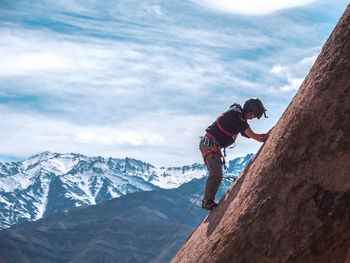 Man climbing on rock formation against snowcapped mountains