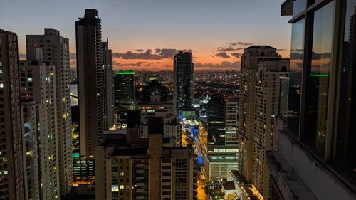 Illuminated buildings in city against sky at sunset