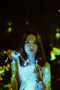 Portrait of beautiful woman holding illuminated string lights at night