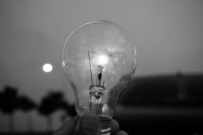 Close-up of hand holding illuminated light bulb against sky