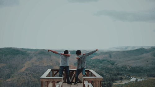 Rear view of men sitting on mountain against sky