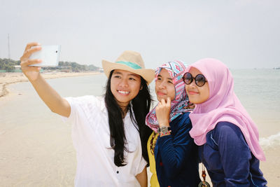 Smiling young women taking selfie while standing at beach