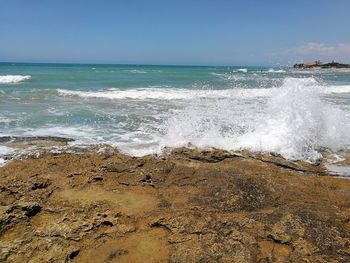 Waves splashing on rocks at beach against sky