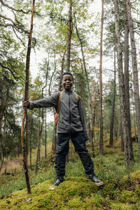 Portrait of smiling boy with stick standing in forest during vacation