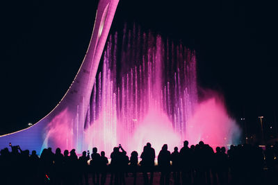 Panoramic view of people looking at firework display at night