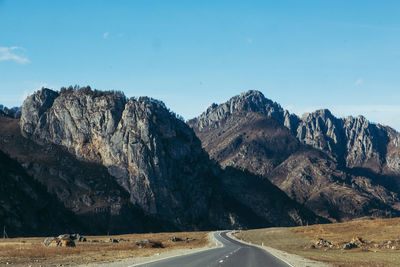 Empty road leading towards mountains against blue sky