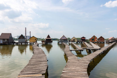 Stilt houses on pier by lake against sky