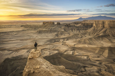 One person standing on rock outcrop in a dramatic desert landscape.