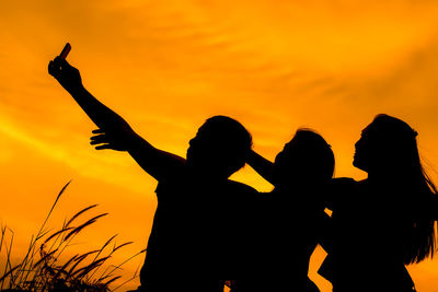 Silhouette friends taking selfie against orange sky