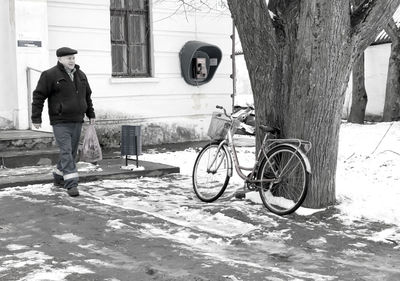 Man with bicycle standing by tree in winter