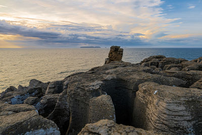 Rocks on beach against sky during sunset