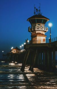 Illuminated pier by sea against sky at night