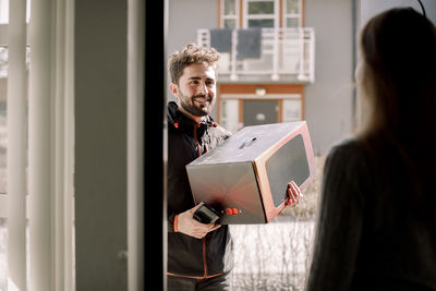 Confident delivery man delivering package to female customer at home