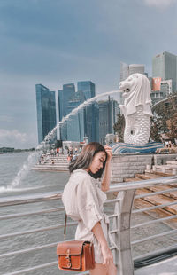 Woman standing by modern cityscape against sky