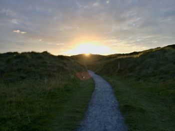 Road amidst field against sky during sunset