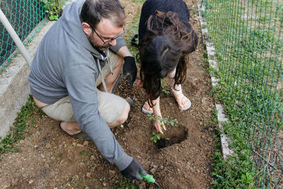 High angle view of father and daughter with long hair planting together seedling in soil