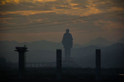 Silhouette man standing by mountain against sky during sunset