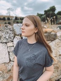 Young woman looking down while standing against stone wall