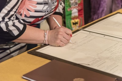 Midsection of woman signing on paper at home