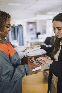 Smiling female delivery person taking digital signature from fashion designer while delivering package