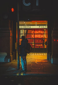 Rear view of woman standing on footpath at night