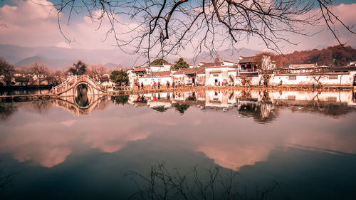 Reflection of houses and trees on river against sky