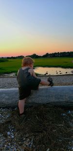 Man sitting by lake against sky during sunset