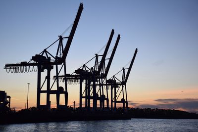 Silhouette cranes by sea against sky during sunset