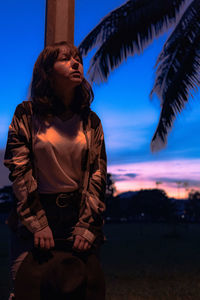 Young woman standing against sky at sunset