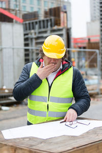 Engineer covering mouth while yawing at construction site