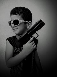 Close-up of boy wearing sunglasses while holding toy gun against wall